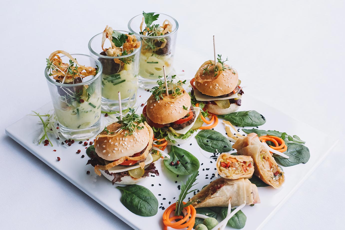 Das Foto zeigt Mini-Burger, frittierte Frühlingsrollen und kleine Bouletten mit Kartoffelsalat im Gläschen.
