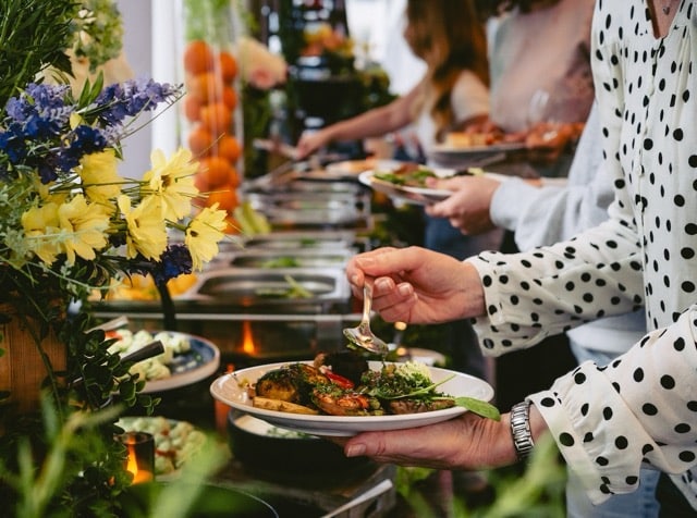 Das Bild zeigt Veranstaltungsgäste, die sich an einem Buffet bedienen.